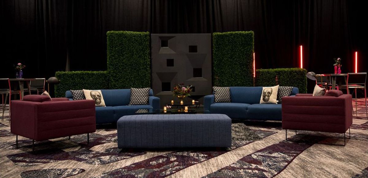 Blue and plum soft seating in front of black dividers and boxwood hedges.