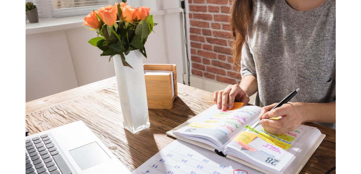 Woman sitting at desk with planner, calendar, and computer.