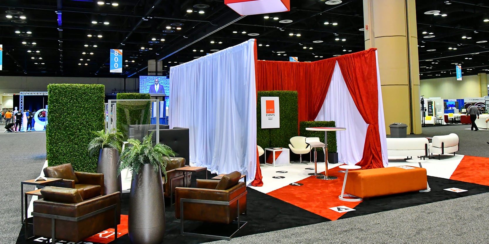 large trade show booth with drape dividers, brown leather seating and orange bench ottomans