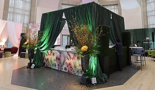 cocktail reception event with stylized bar with customized graphic panels surrounded by green drape with uplighting
