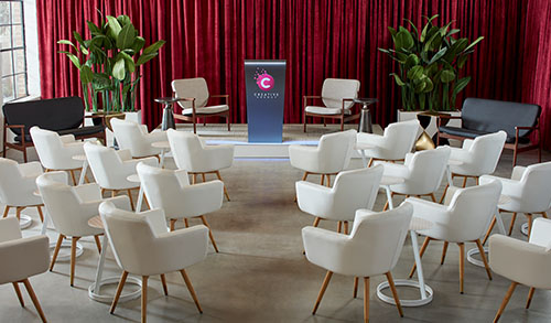 meeting with rows of black guest chairs, accent chairs with a lectern on stage and red drape backdrop